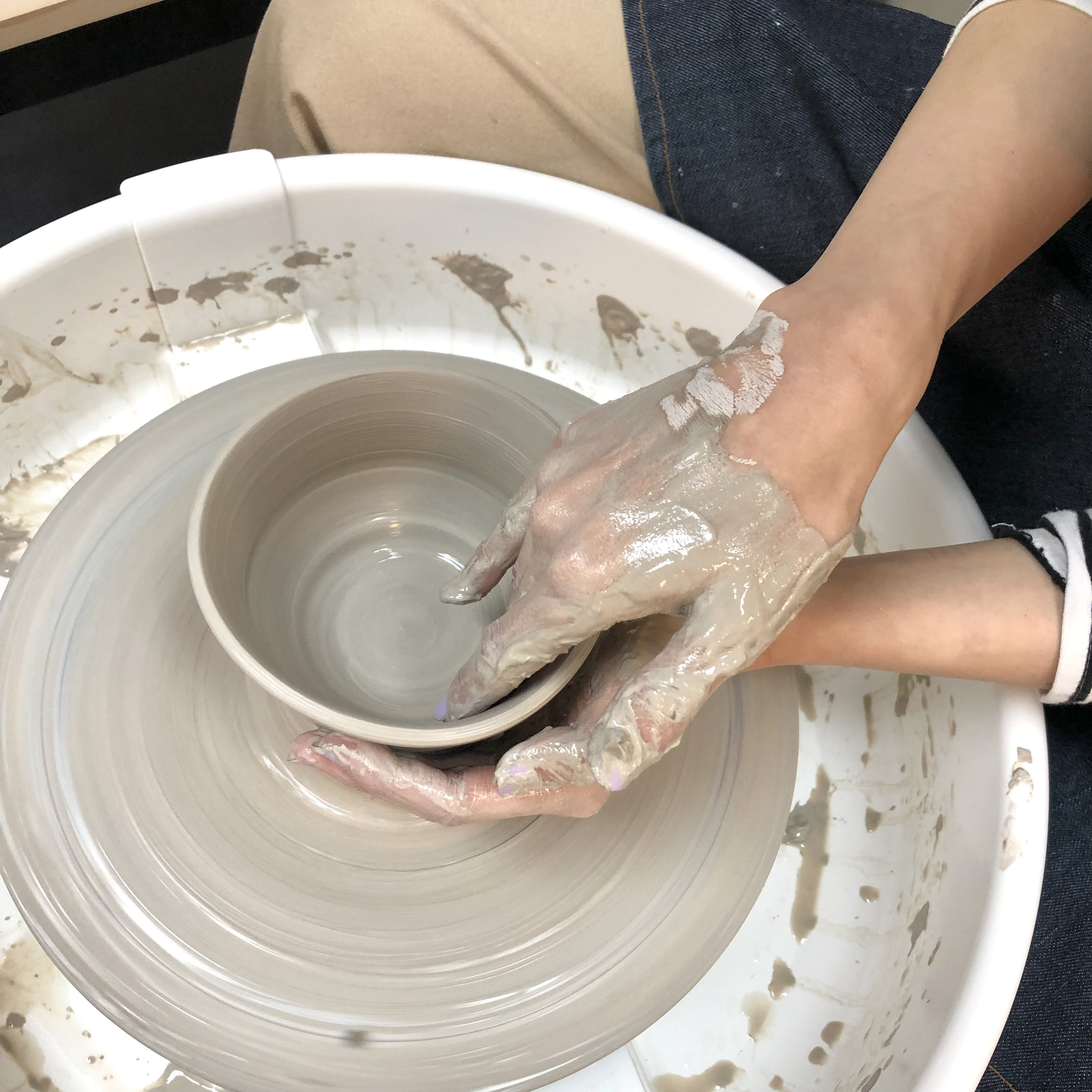 Hands shaping clay on a pottery wheel